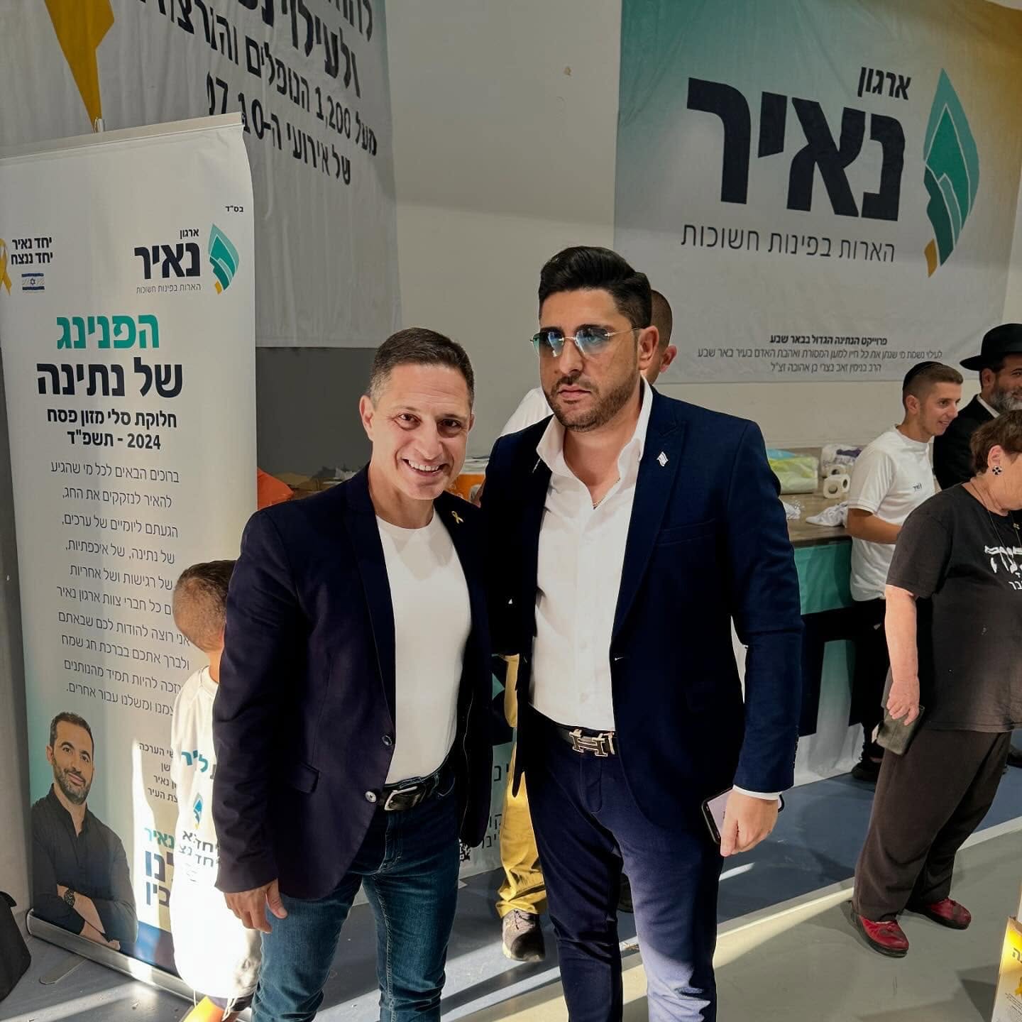 אדם שטרית עומד לצד משתתף בפעילות ליד שלטי ארגון נאיר