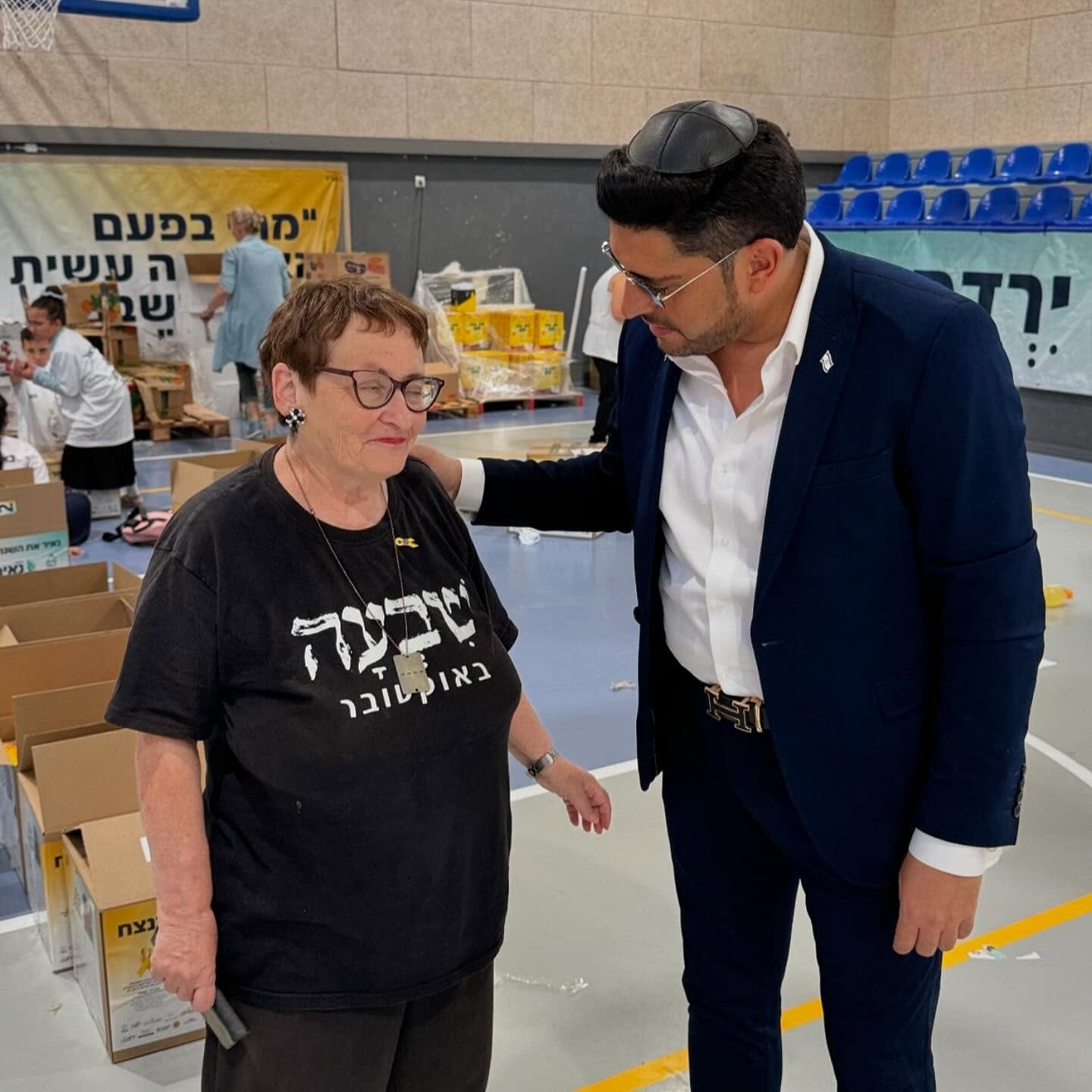 אדם שטרית משוחח עם משתתפת באולם שבו נארזים סלי מזון