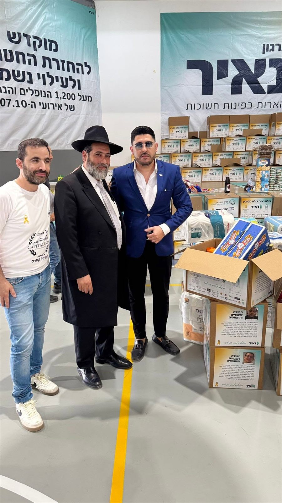 אדם שטרית ומשתתפים עומדים ליד סלי מזון ושלטי ארגון נאיר
