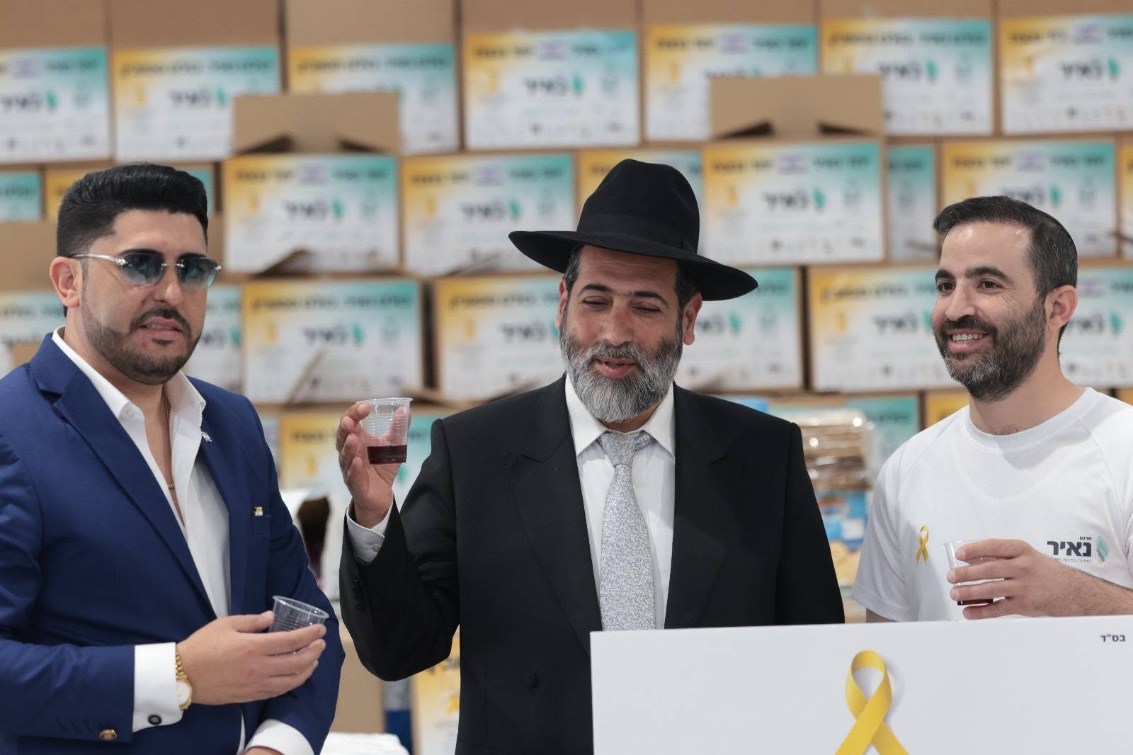 שלושה משתתפים עומדים לפני שורות של סלי מזון ארוזים
